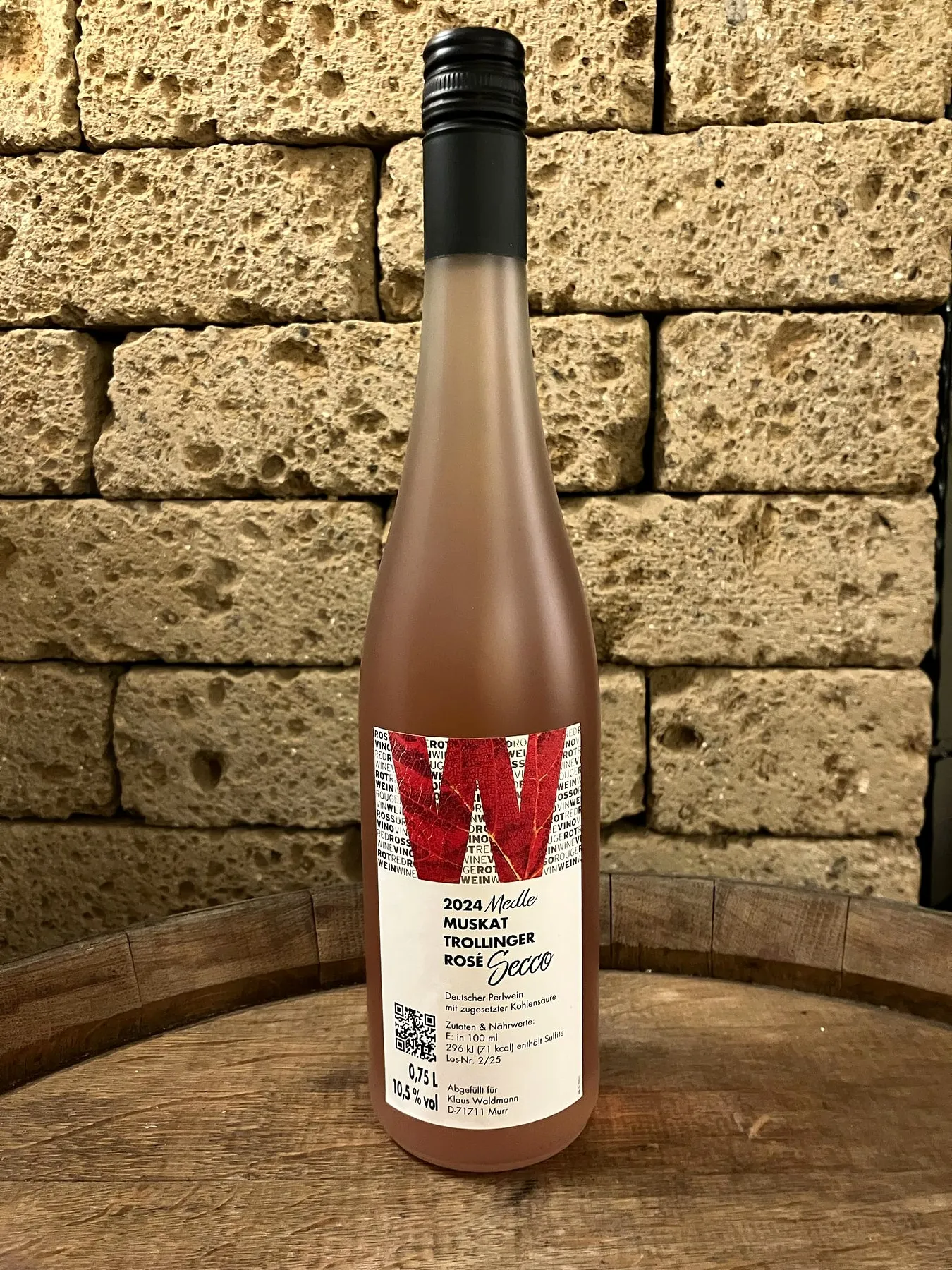 Flasche Muskattrollinger Rosé Secco vor der Muschelkalkwand, das W auf dem Etikett ist ein herbstrotes Rebblatt