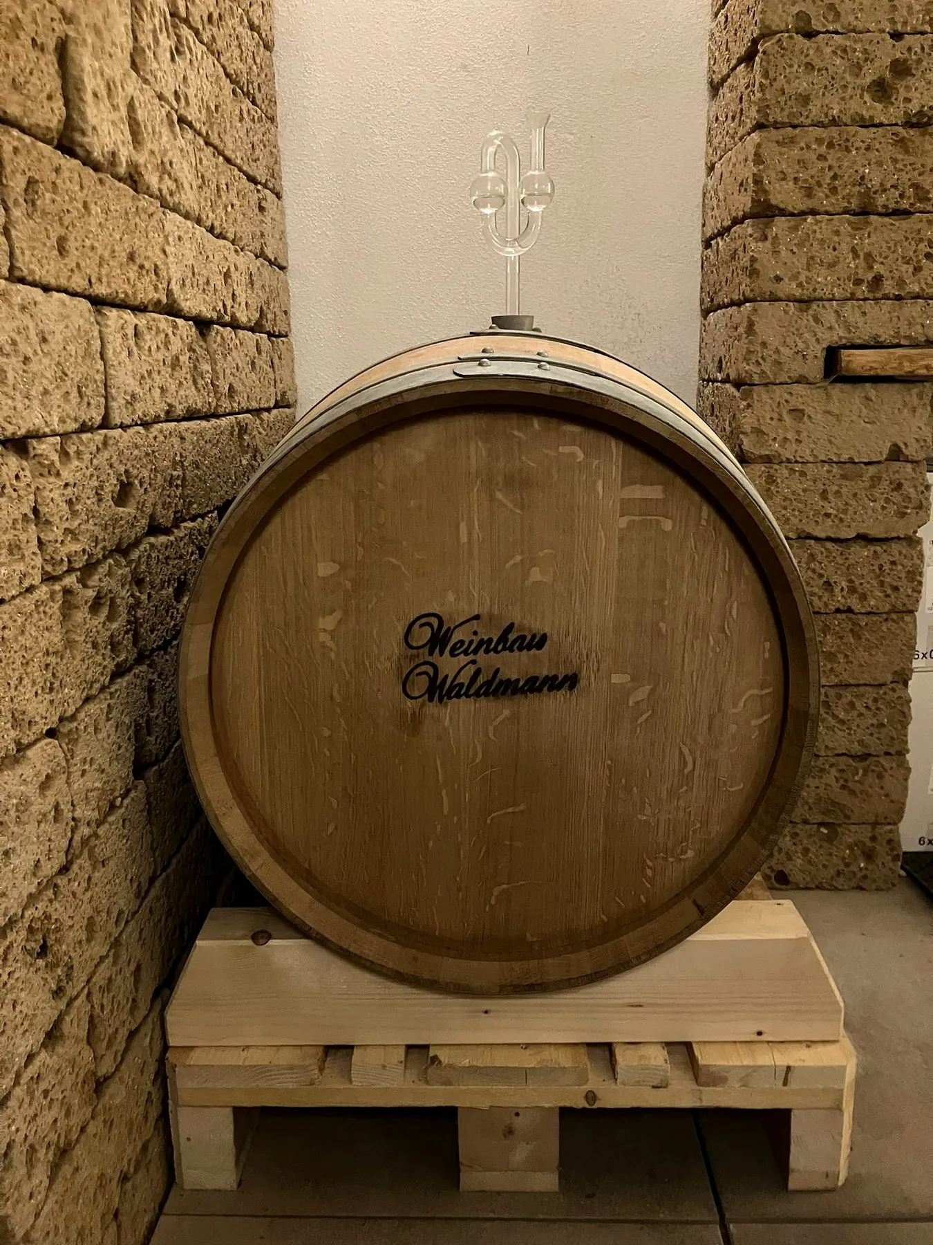 Holzfass mit eingebranntem Schriftzug Weinbau Waldmann, auf einer Palette vor der Muschelkalkwand